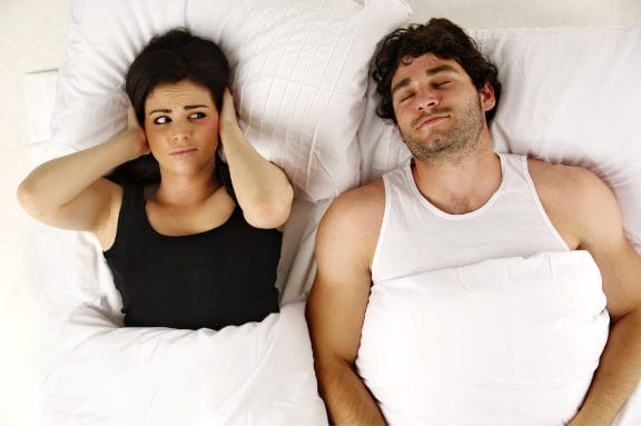 Couple laying in bed with woman covering her ears