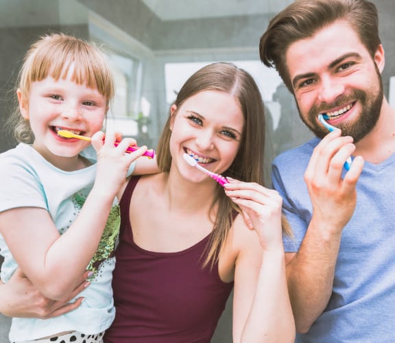 Family of three looking in the mirror and brushing their teeth together