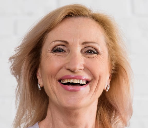 Older woman standing in front of a brick wall and smiling